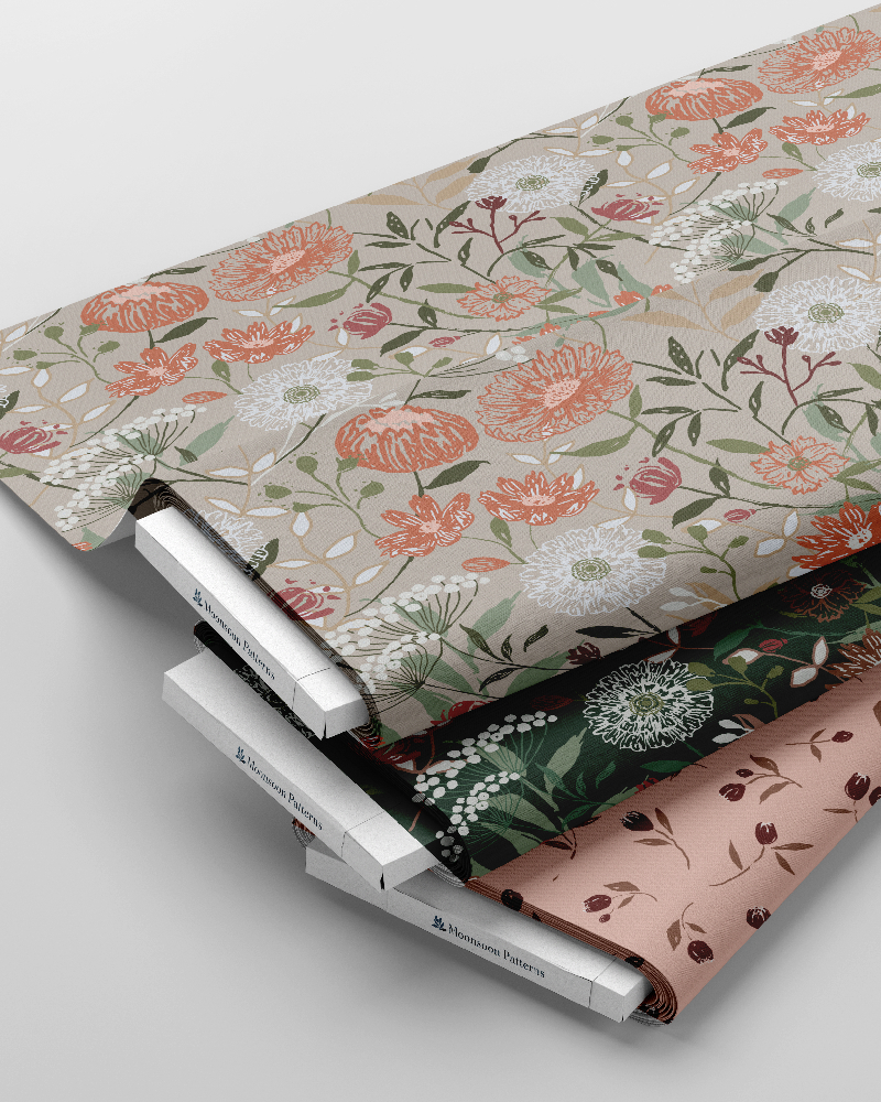 Atelier Botanique pattern collection by Moonsoon Patterns displayed on fabric rolls featuring floral botanical designs in muted green, coral, blush and blue