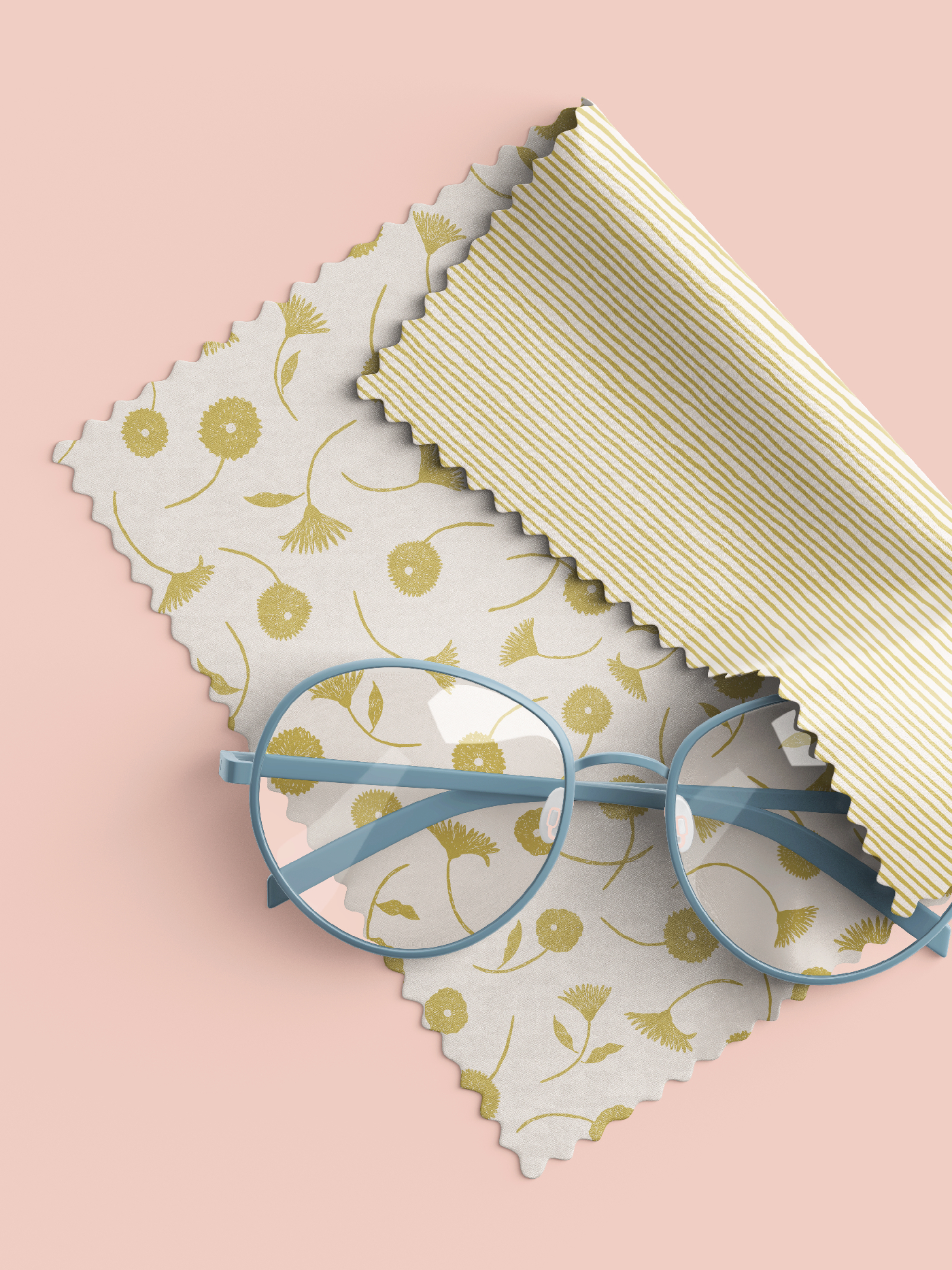 Folded eyeglass cleaning cloth featuring the Dancing Blooms Tonal floral pattern in a soft green Heritage Garden colorway, styled with blue-framed glasses.