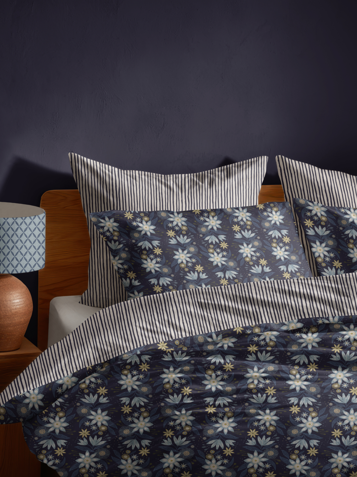 Layered bedding featuring the Garden Reverie floral pattern in deep navy, paired with coordinating blue and ivory striped pillows and sheets.