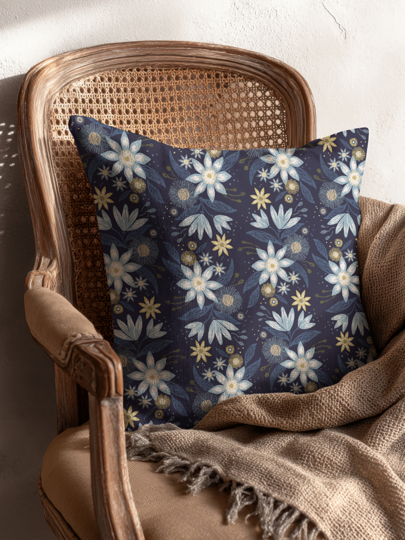Woven armchair with a decorative floral cushion featuring the Garden Reverie pattern in the Heritage Garden colorway, styled with a soft brown throw.