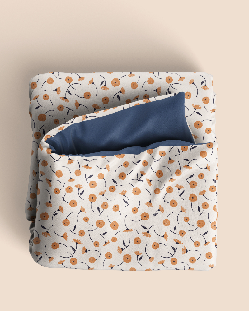 Folded duvet featuring the Dancing Blooms floral pattern from the Botanical Reverie collection in the Heritage Garden colorway, with delicate orange flowers and dark blue stems on a warm ivory background.